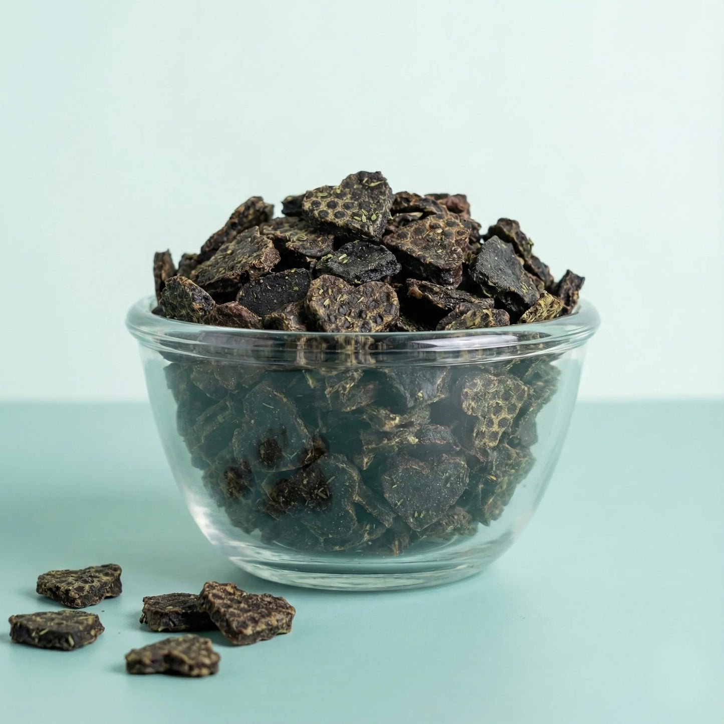 Clear glass bowl filled with Oscar Daisy dog treats in a light blue background