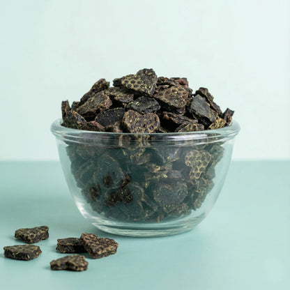 Clear glass bowl filled with Oscar Daisy dog treats in a light blue background