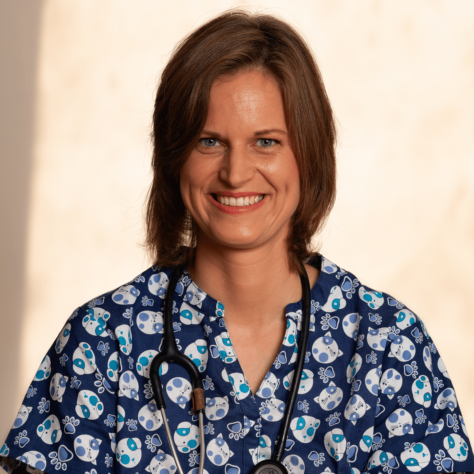 Dr.Juliet wearing a blue patterned shirt with a stethoscope around their neck on a beige background