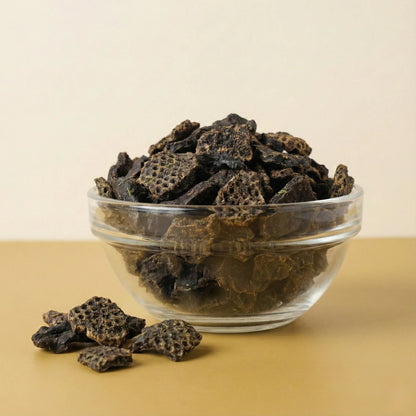 Glass bowl filled with dark brown healthy dog treats on a beige background