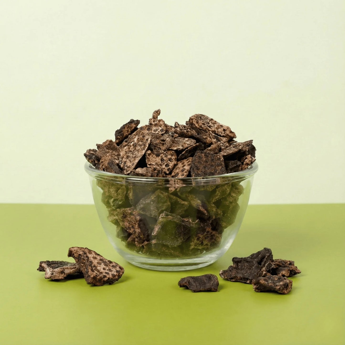Glass bowl filled with Oscar Daisy Liver Pirandai dehydrated dog treats showing brown liver pieces and green pirandai cubes on green backdrop