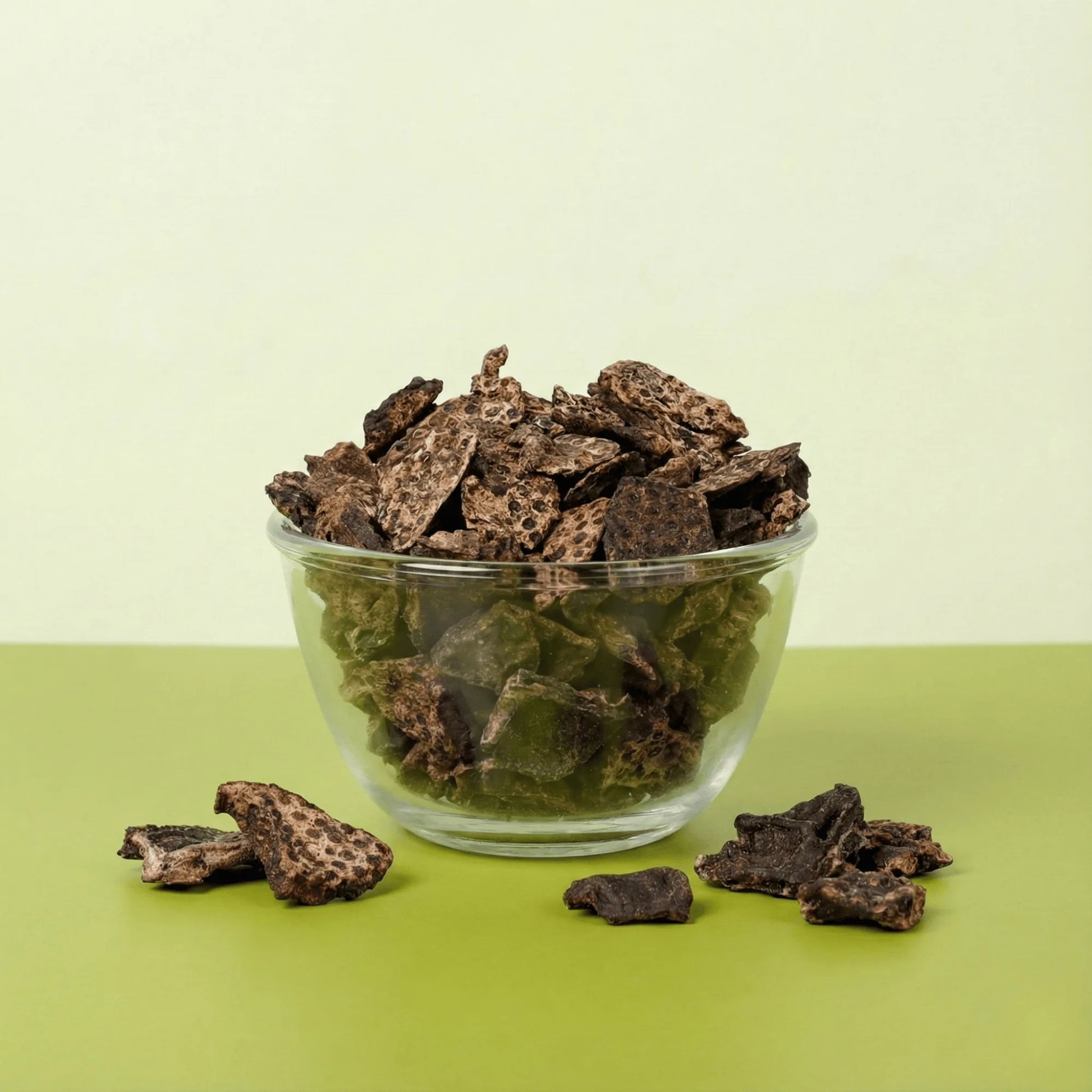 Glass bowl filled with Oscar Daisy Liver Pirandai dehydrated dog treats showing brown liver pieces and green pirandai cubes on green backdrop