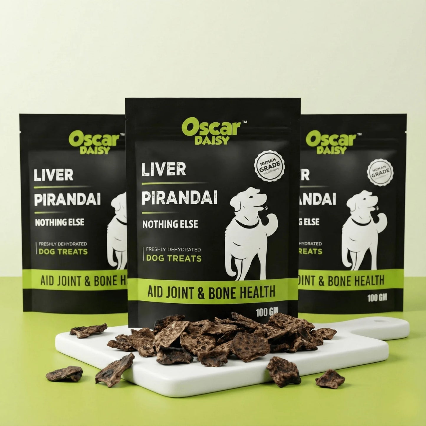 Multiple Oscar Daisy Liver Pirandai dog treat pouches standing behind white board piled with dehydrated treats on green surface